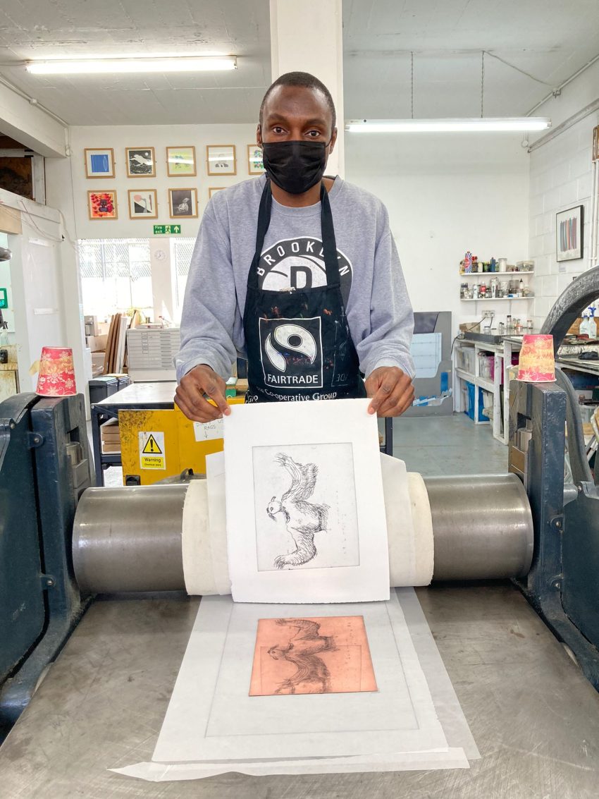 Artist Adam Crown wearing a face mask and holding a print of his artwork titled 'The Blackbird', 2022
