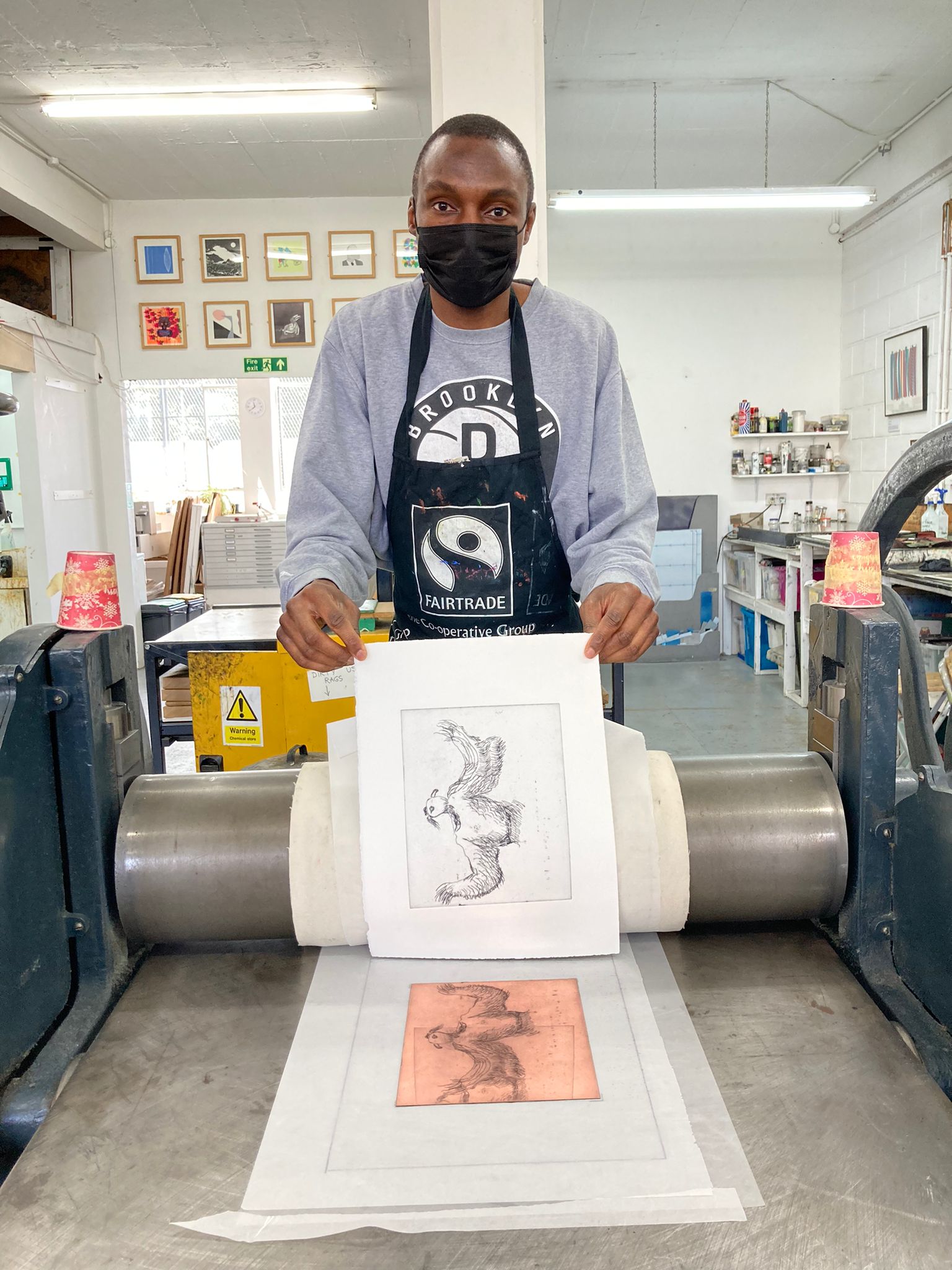 Artist Adam Crown wearing a face mask and holding a print of his artwork titled 'The Blackbird', 2022