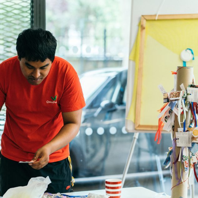 A man wearing a red t-shirt painting in a studio.