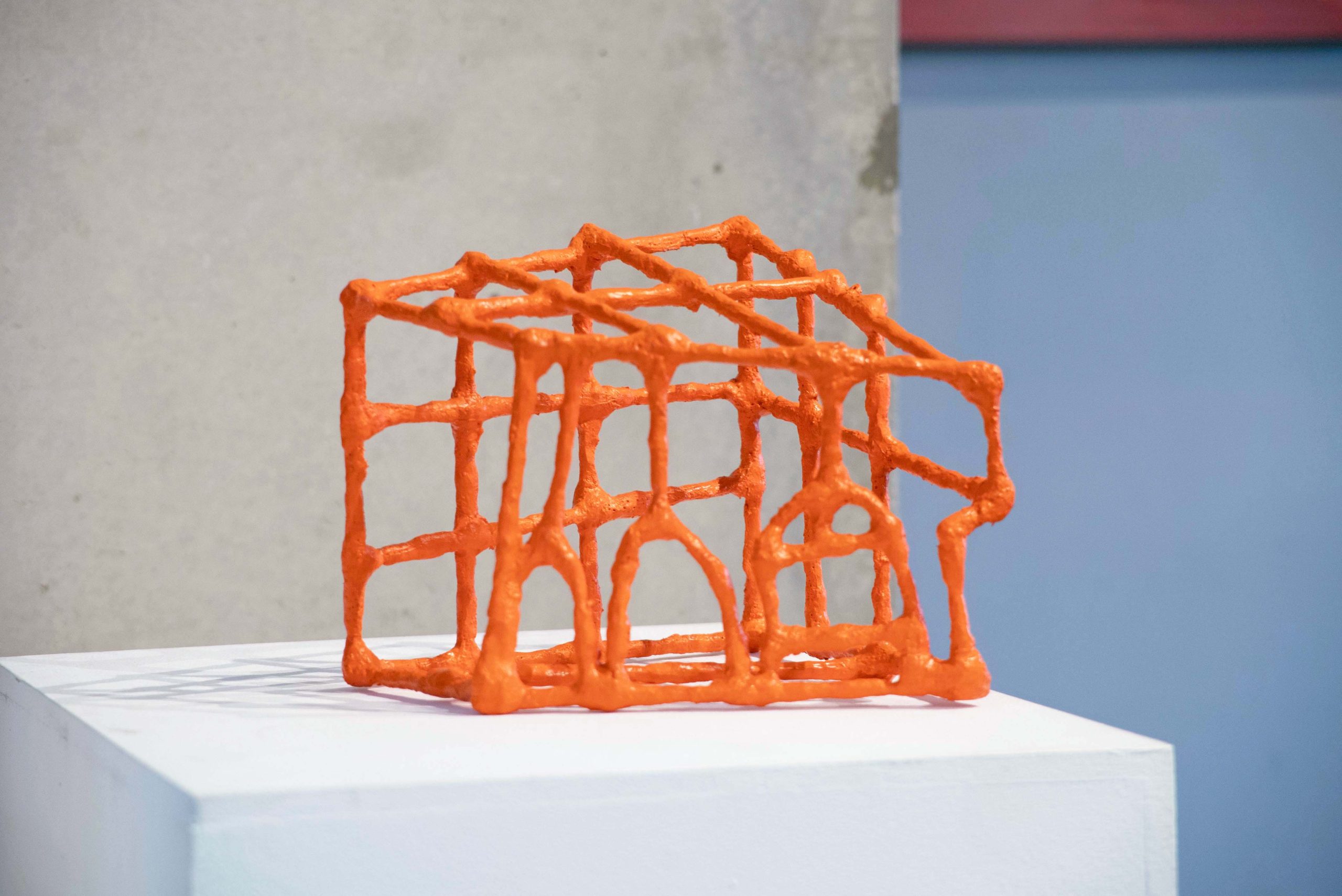 A small orange sculpture with thick constructed lines in an abstract shape.