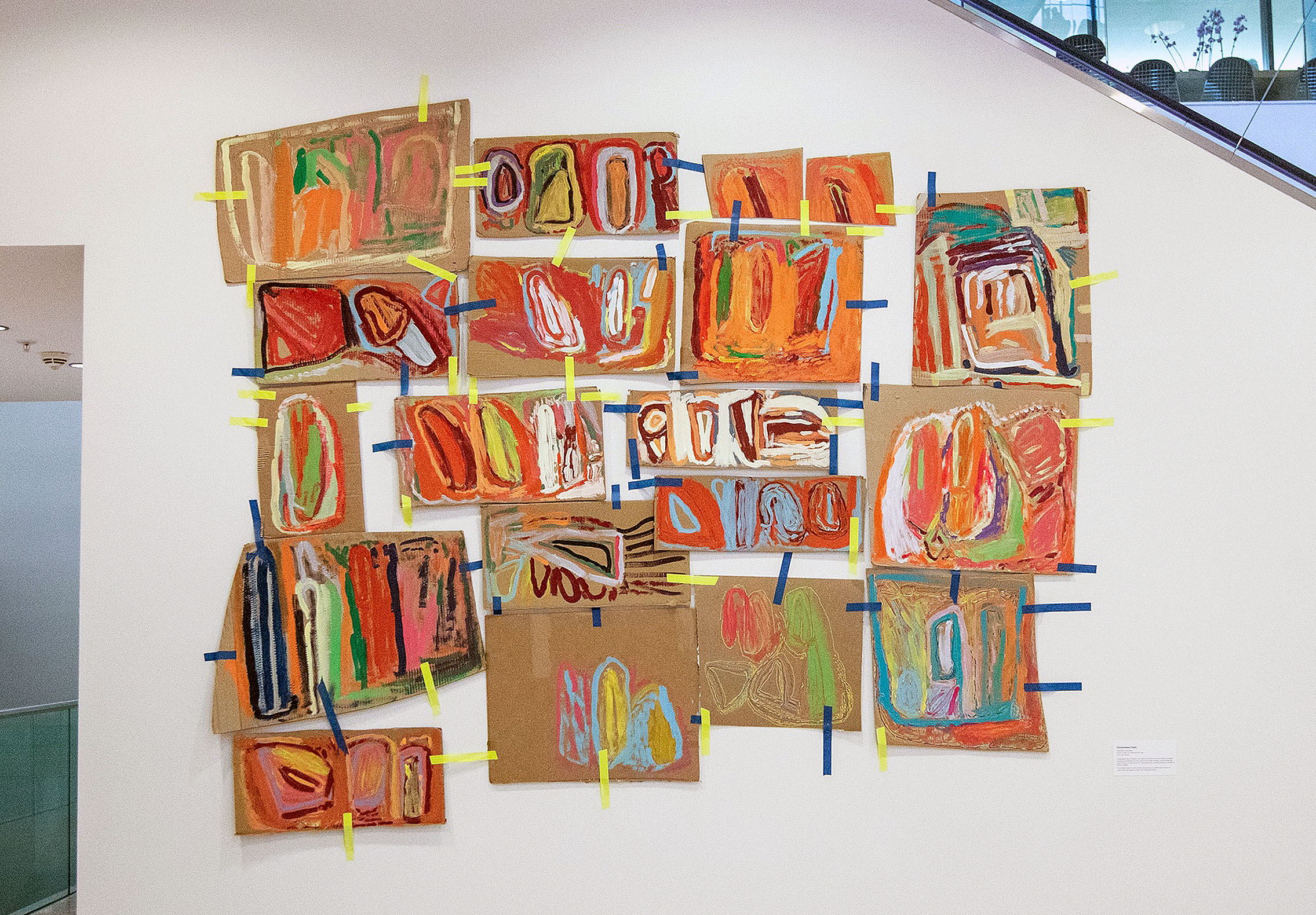 Installation view of multiple paintings hung up with coloured tape.