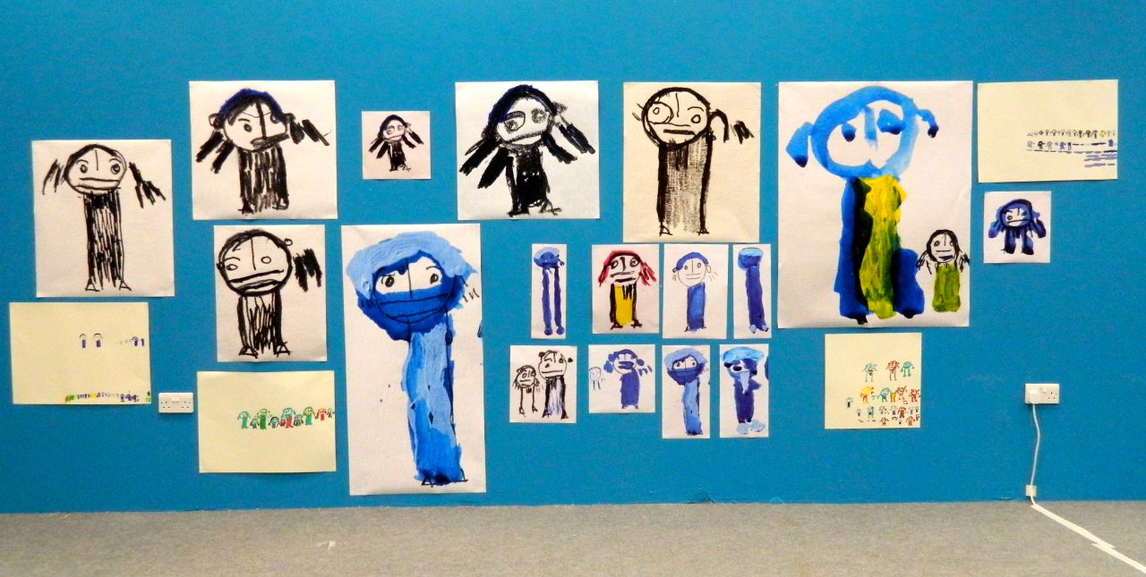 Installation view of a series of drawings of people on a blue wall.