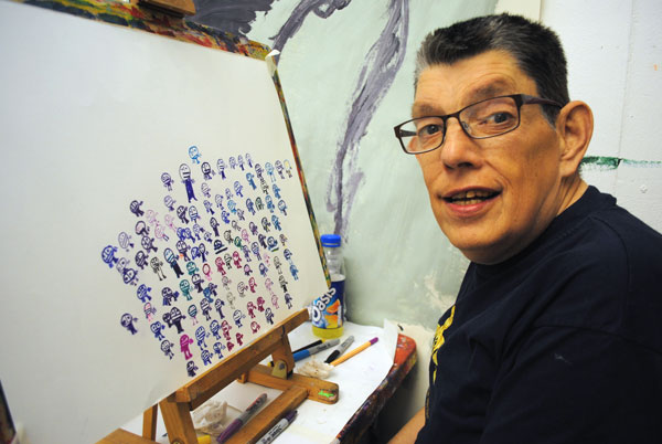 A man wearing a black jumper sat at an easel drawing.