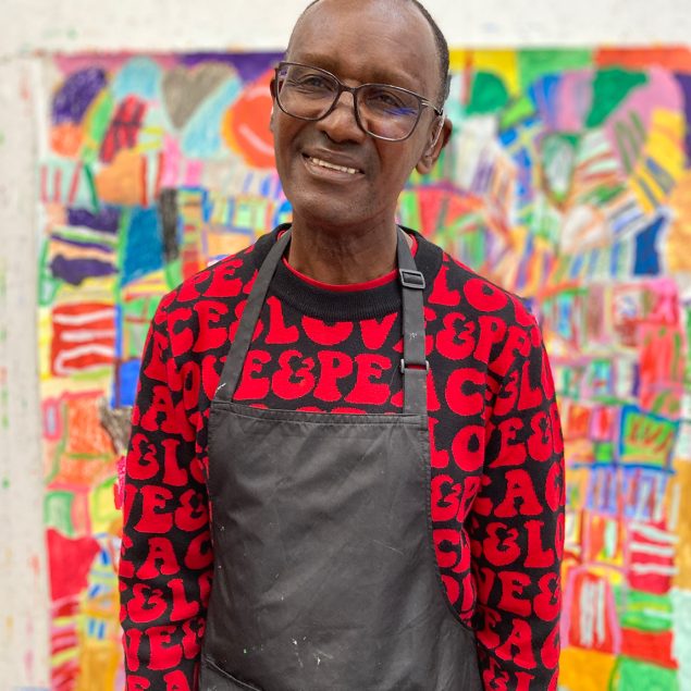 Artist Derek Williams standing in front on his abstract painting. He is wearing a red and black jumper.