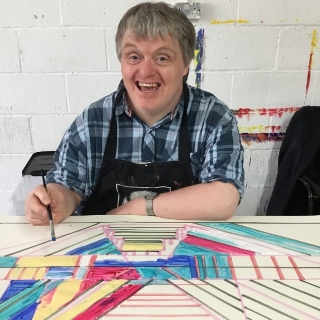 A man smiling at the camera with a paintbrush in his hand.