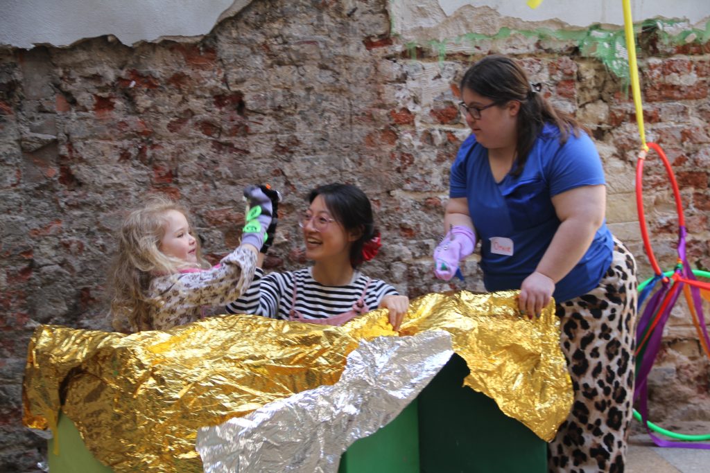 Ophir Yaron with participants at her workshop. She is with a woman and a child, standing next to a table that has a sheet of gold foil on it.