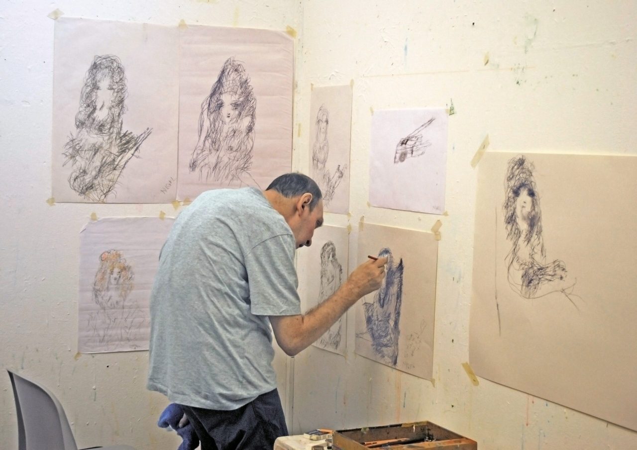 The artist standing in the studio surrounded by his drawings. Nigel is standing at the wall drawing.