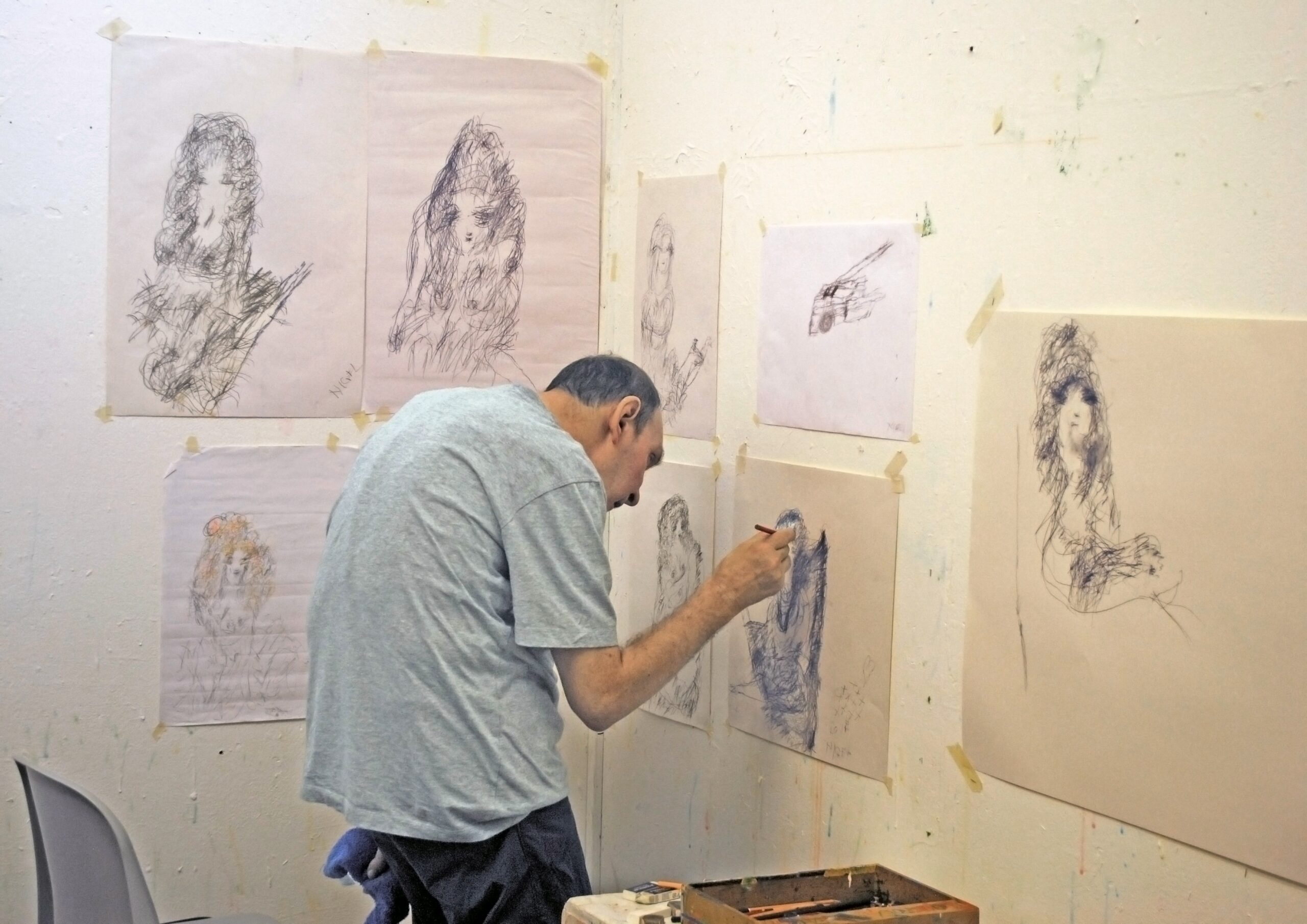 The artist standing in the studio surrounded by his drawings. Nigel is standing at the wall drawing.