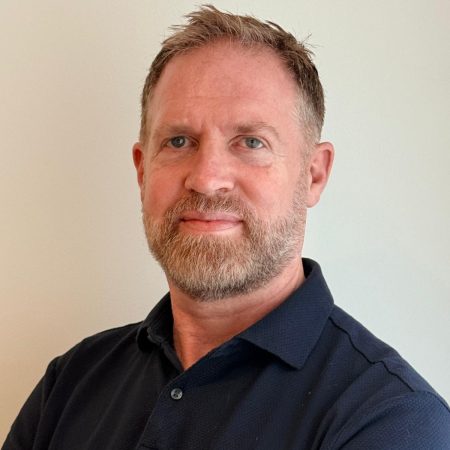 A photo of Neil Debnam. A white man with short brown hair and a short beard. He is wearing a dark coloured polo shirt.