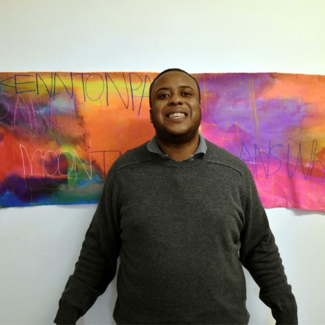 A man standing and smiling in front of his artwork.