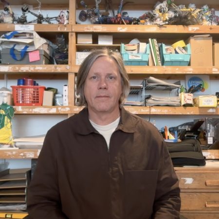 A picture of Dan Lamont. He is a white man with mid length grey air. He is wearing a brown shirt with a white t shirt and is seated in front of some shelves in ActionSpace's office.