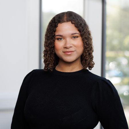 A woman of mixed Black Caribbean and White heritage, she has shoulder length dark hair and is wearing a black top.