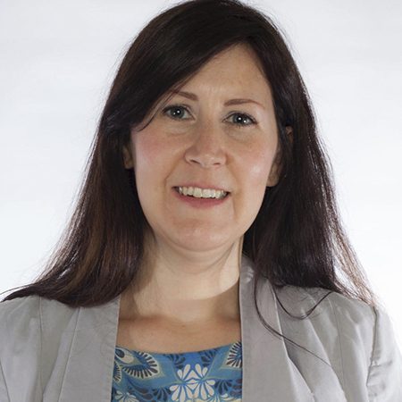 A picture of Fleur Donnely-Jackson. She is a white woman with long dark hair. She is wearing a grey suit jacket and a floral top.