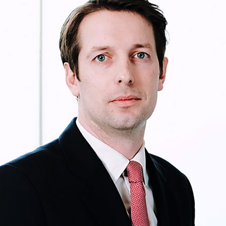 A pcture of Simon Chadwick. He is a white man with short brown hair, he is wearing a dark suit, a white shirt and a red tie.