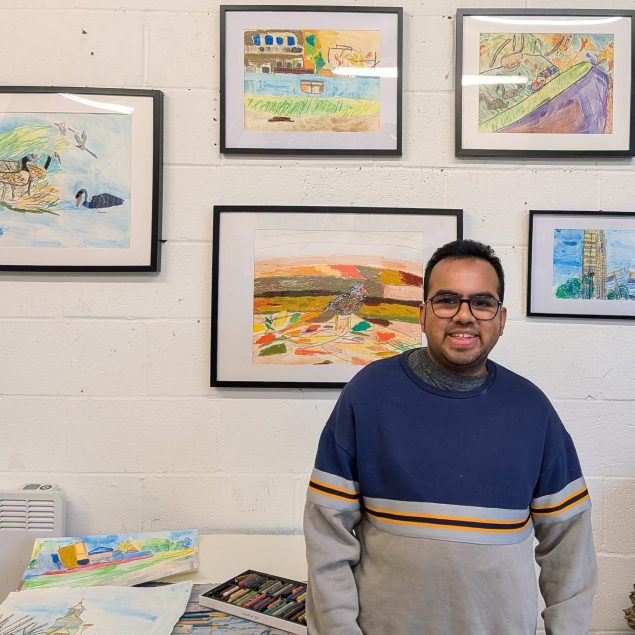 Artist Arvindh Ganesh standing in front of a wall of his framed artworks.