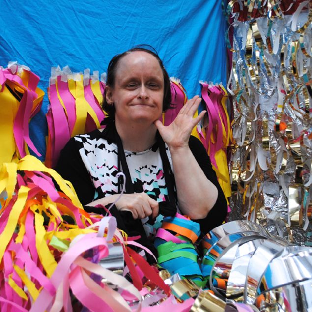 Artist Linda Bell sat in amongst her sculptural artwork made up of strips of yellow and pink paper and silver foil.