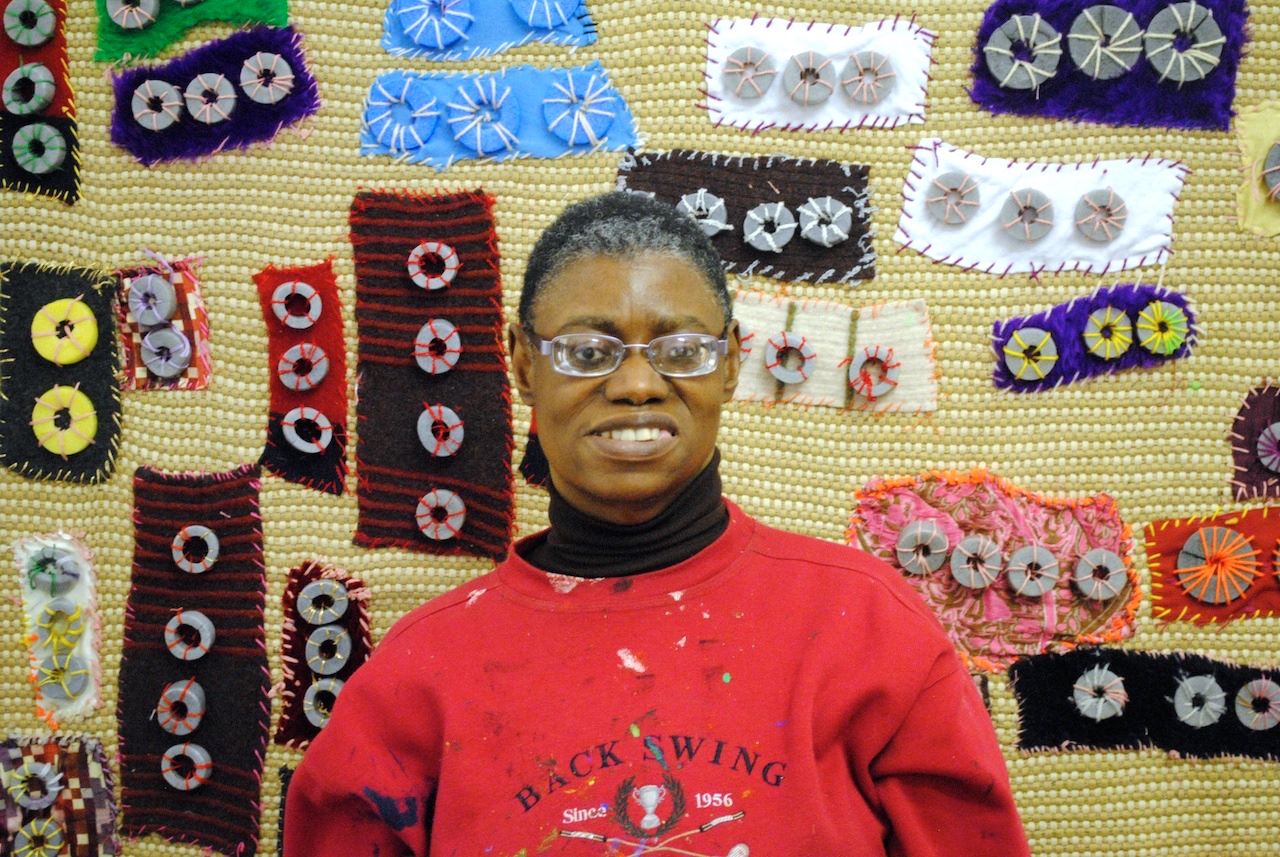 Artist Lasmin Salmon wearing a red jumper and standing in front of her artwork.