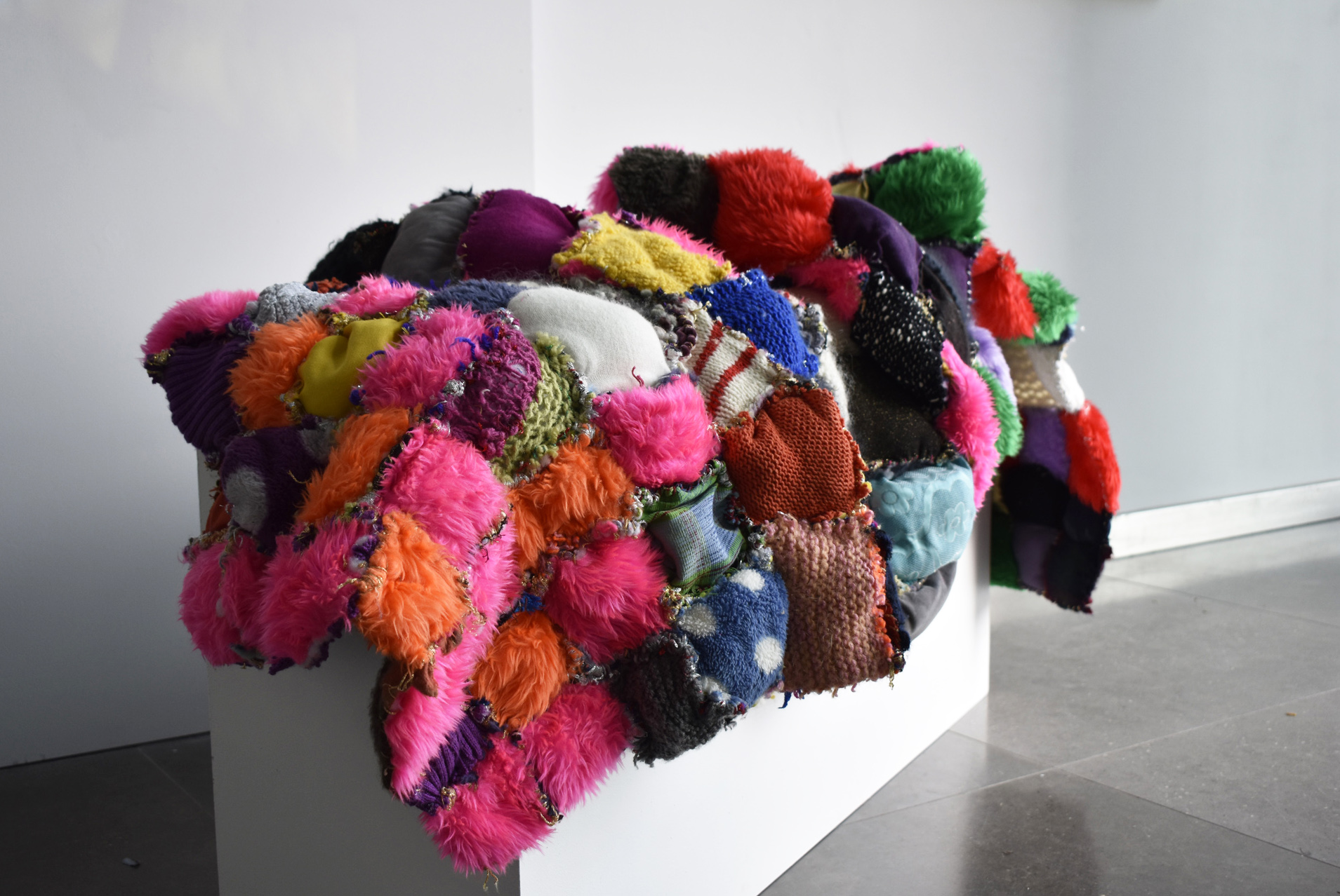 A patchwork multicoloured quilt laying across a white plinth.