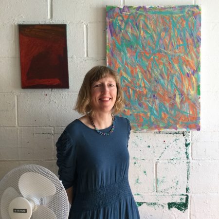 A picture of Flora Bain. A white woman with mid length light brown hair. She is wearing a blue dress and standing in ActionSpace's Cockpit studio.