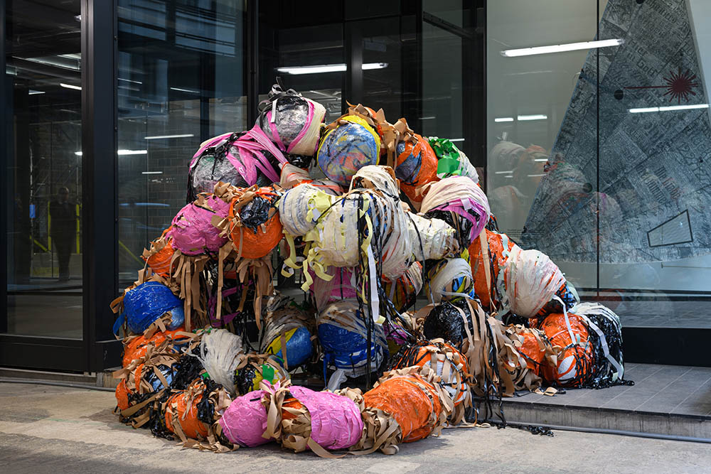 A large multimedia sculpture in an industrial gallery space made up of segmented wrapped parts.