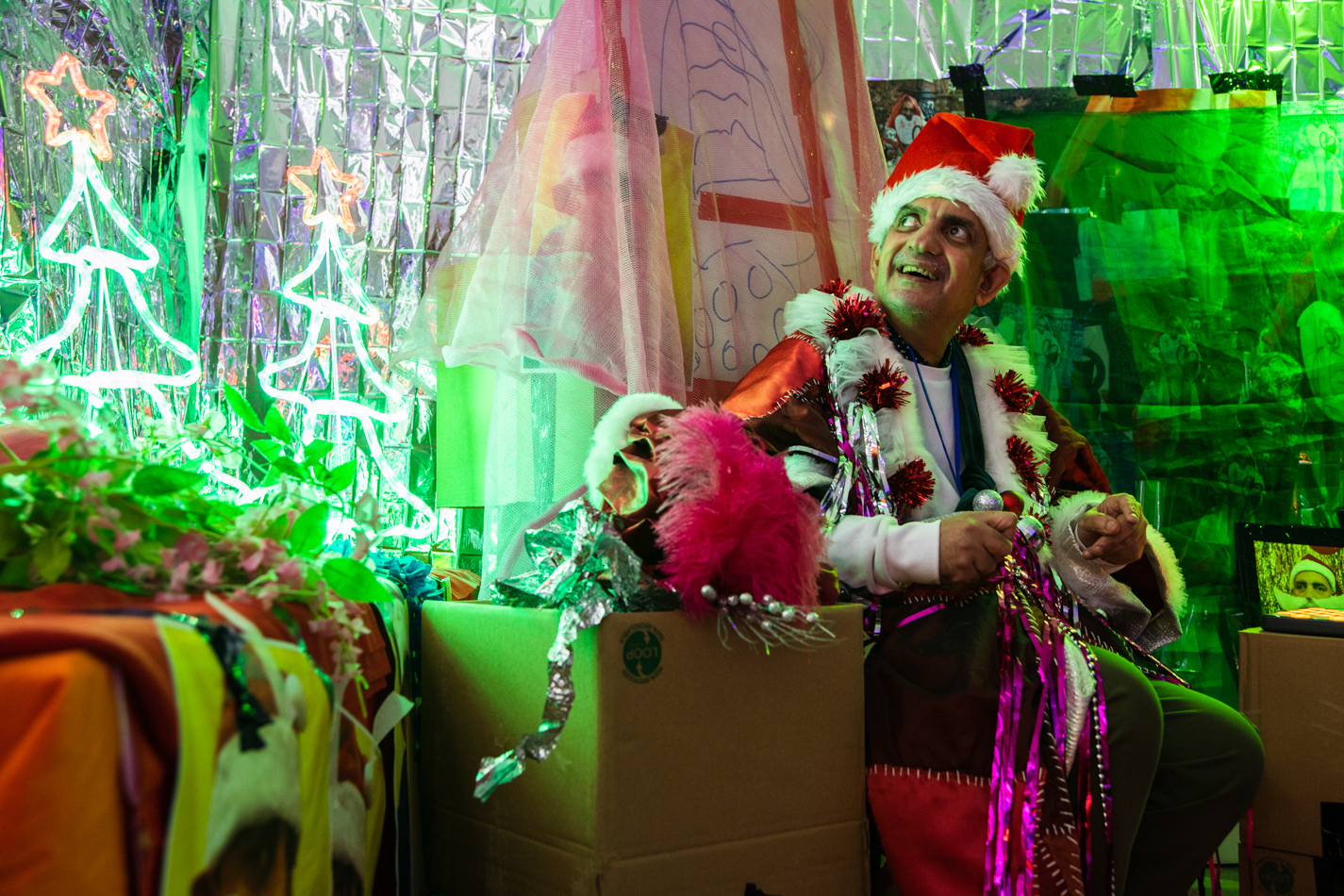 Artist Pardip Kapil, wearing a Santa hat and DIY jacket, sits within a makeshift den.