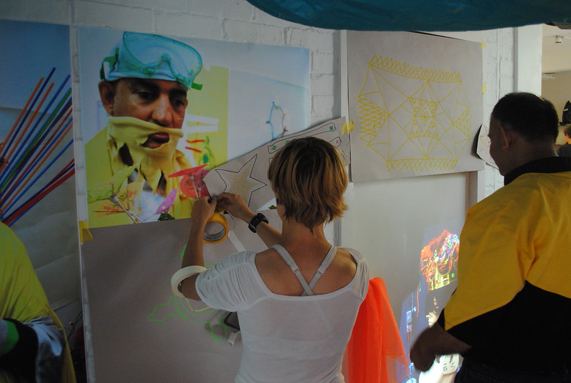 Two people hanging paper artworks with tape on the wall.
