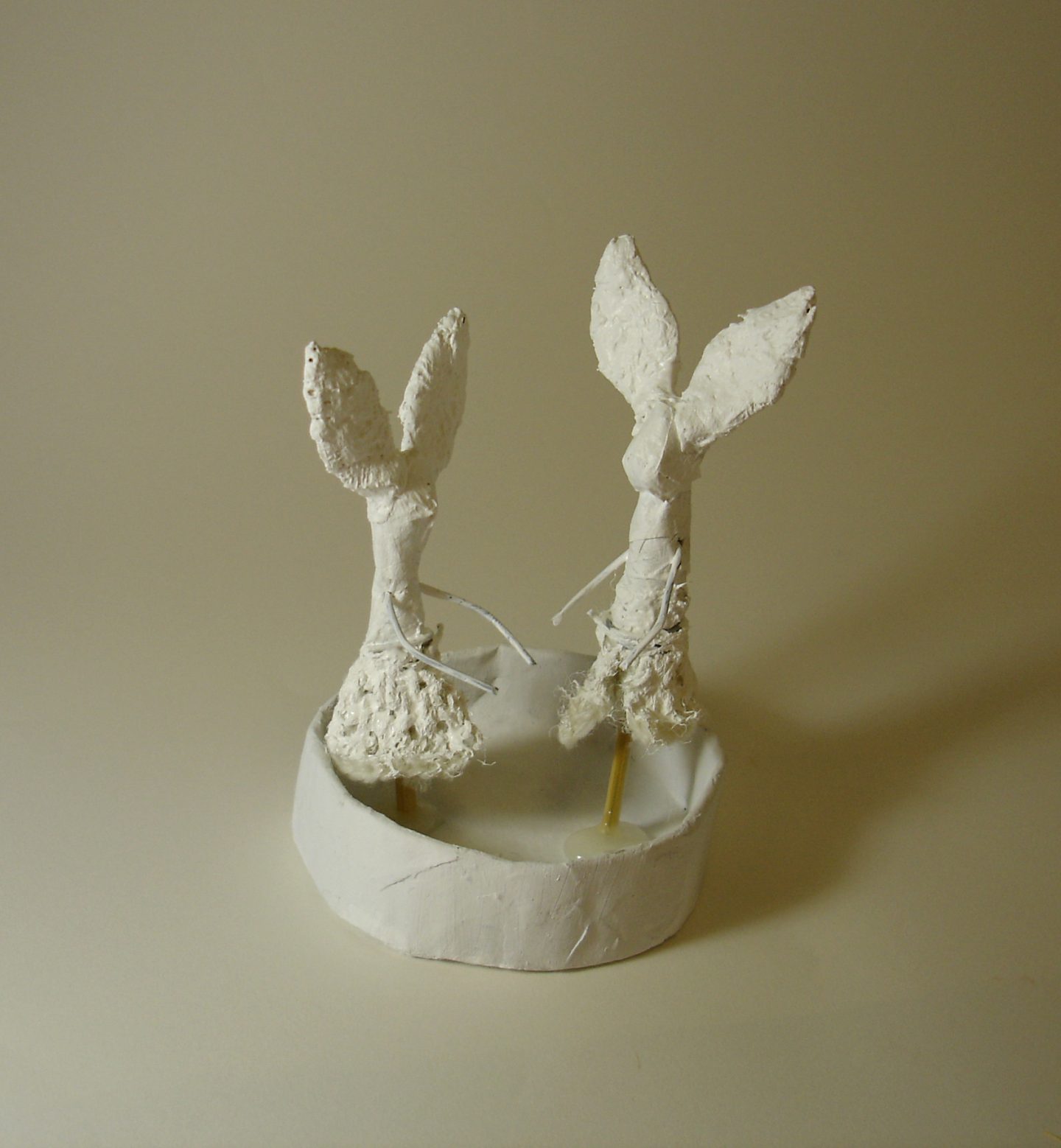A small, white mixed media sculpture of two fish tails coming out of a dish.