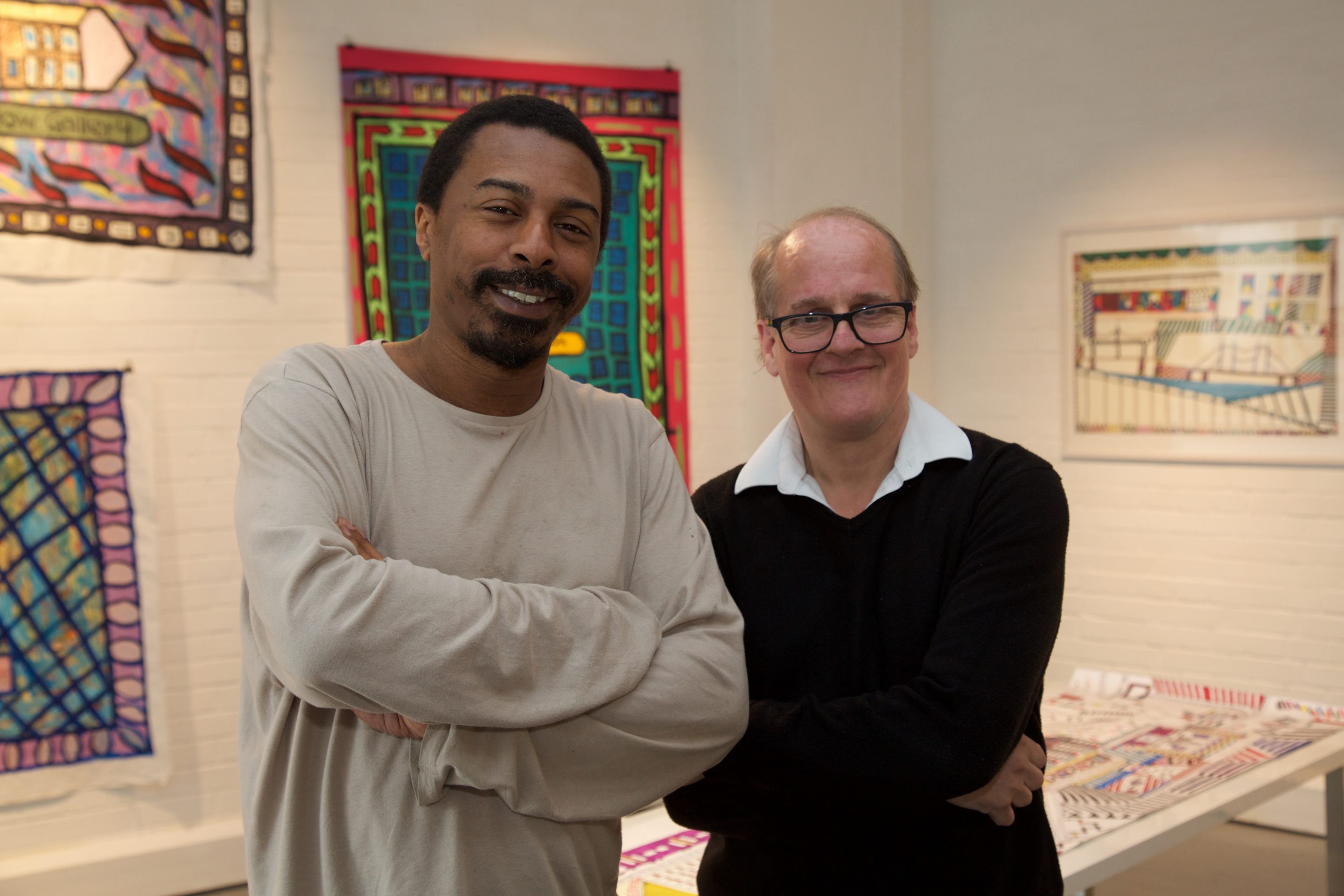 Artists Thompson Hall and Ian Wornast pose together with crossed arms in front of their exhibition.