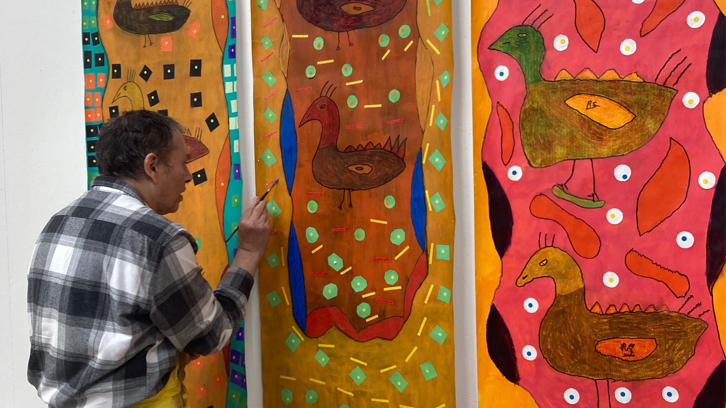 Artist Robin Smith standing up painting. He is wearing a check shirt.