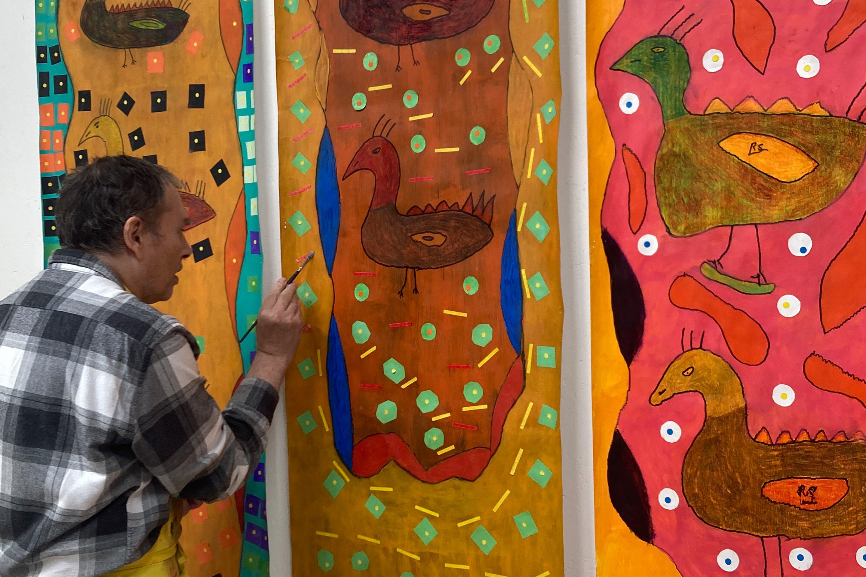 Artist Robin Smith standing up painting. He is wearing a check shirt.