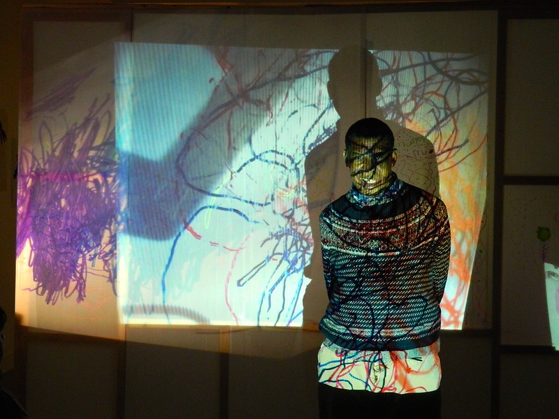 A man stood in front of projected abstract art.