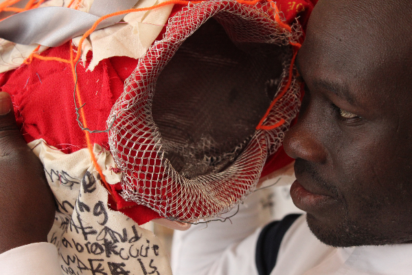 Andrew Omoding looks into some of his fabric artwork, his face touching it.