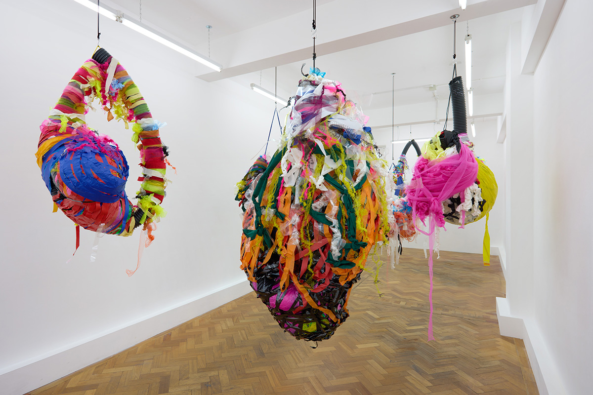 Three colourful, large mixed media sculptures hung from the ceiling in an exhibition.