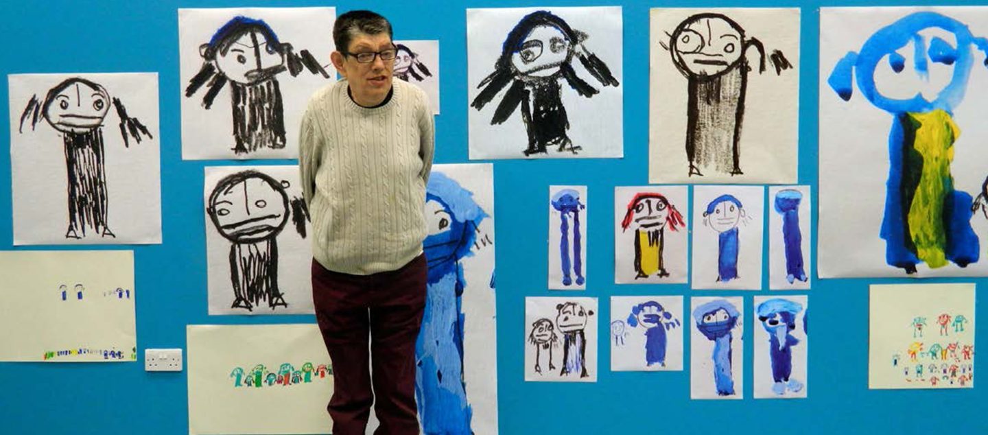 Roland Young in front of his artworks hung on a cerulean blue wall.