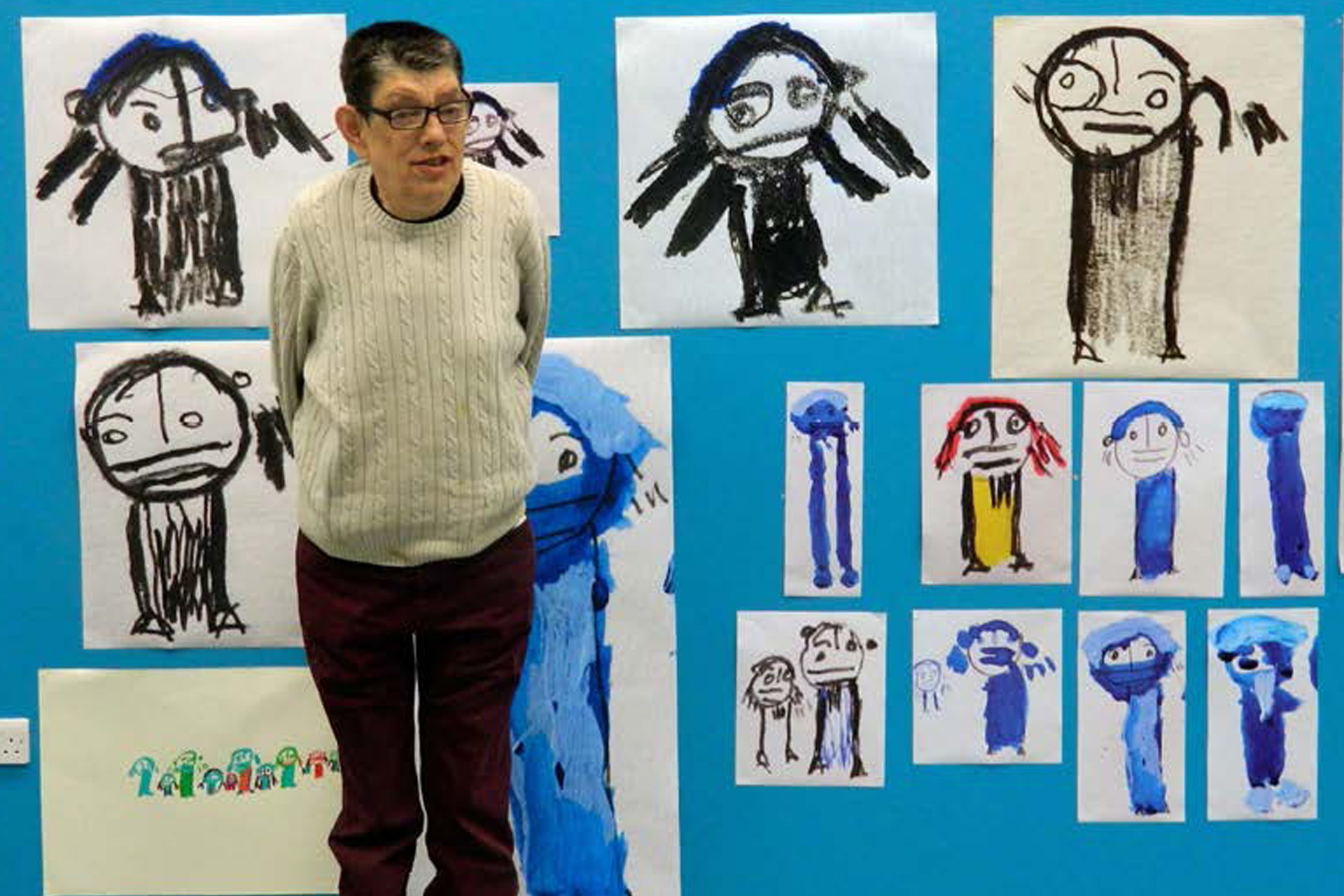 Roland Young in front of his artworks hung on a cerulean blue wall.