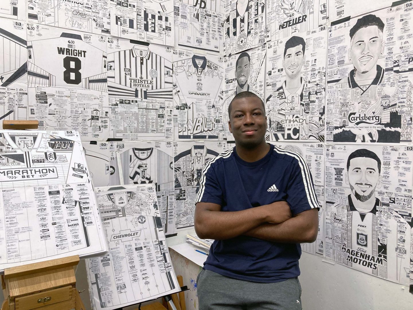 Artist Babajide Brian poses with his arms folded in front of his artwork in his studio space.