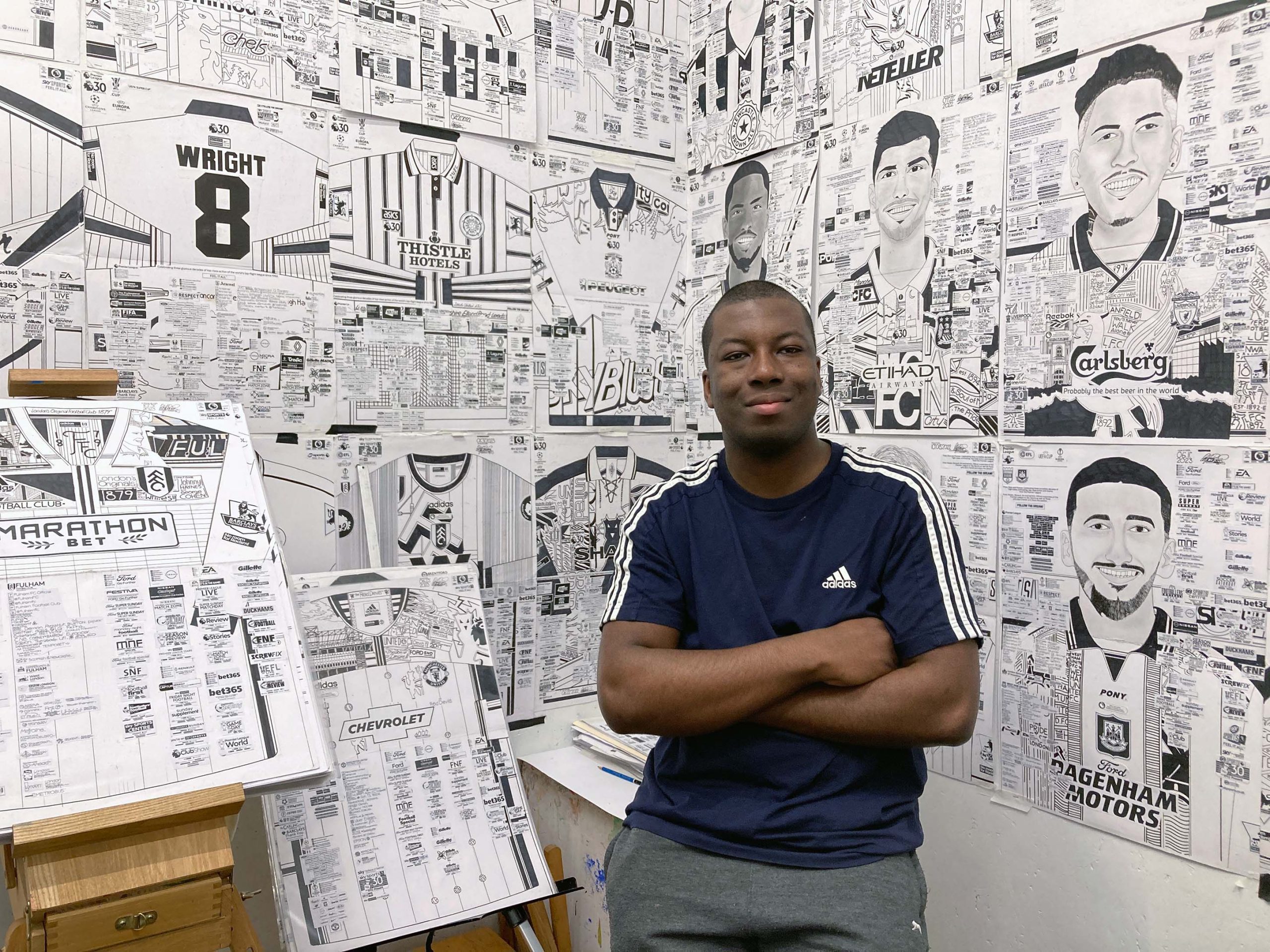 Artist Babajide Brian poses with his arms folded in front of his artwork in his studio space.