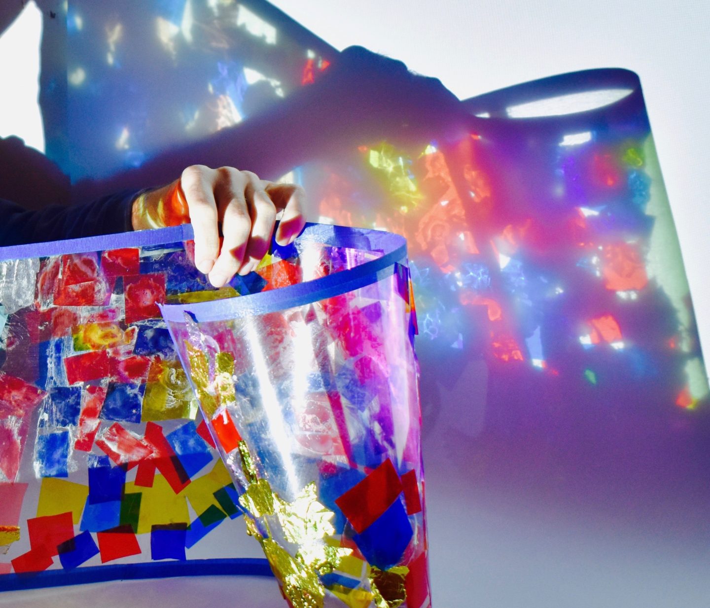A hand holding up an acetate artwork with light projecting it against a wall.