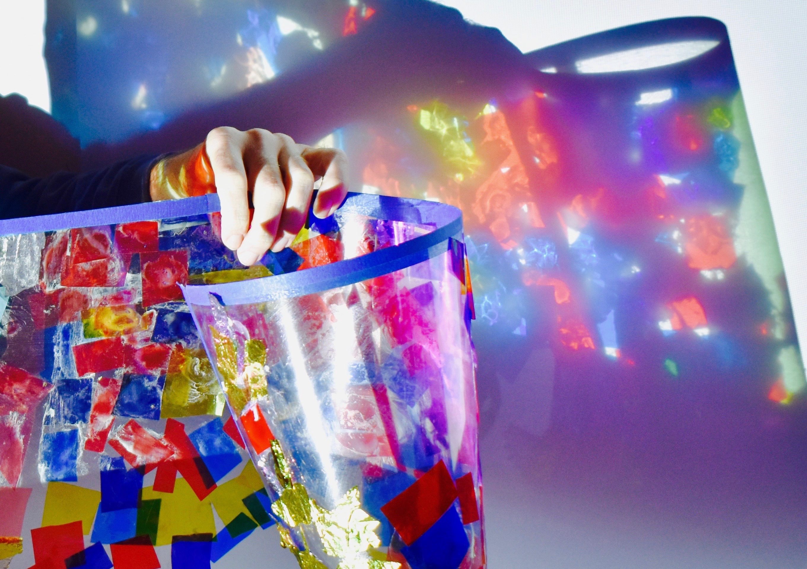 A hand holding up an acetate artwork with light projecting it against a wall.