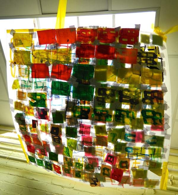 Layers of printed coloured acetates hung in a square, in front of a ceiling window.