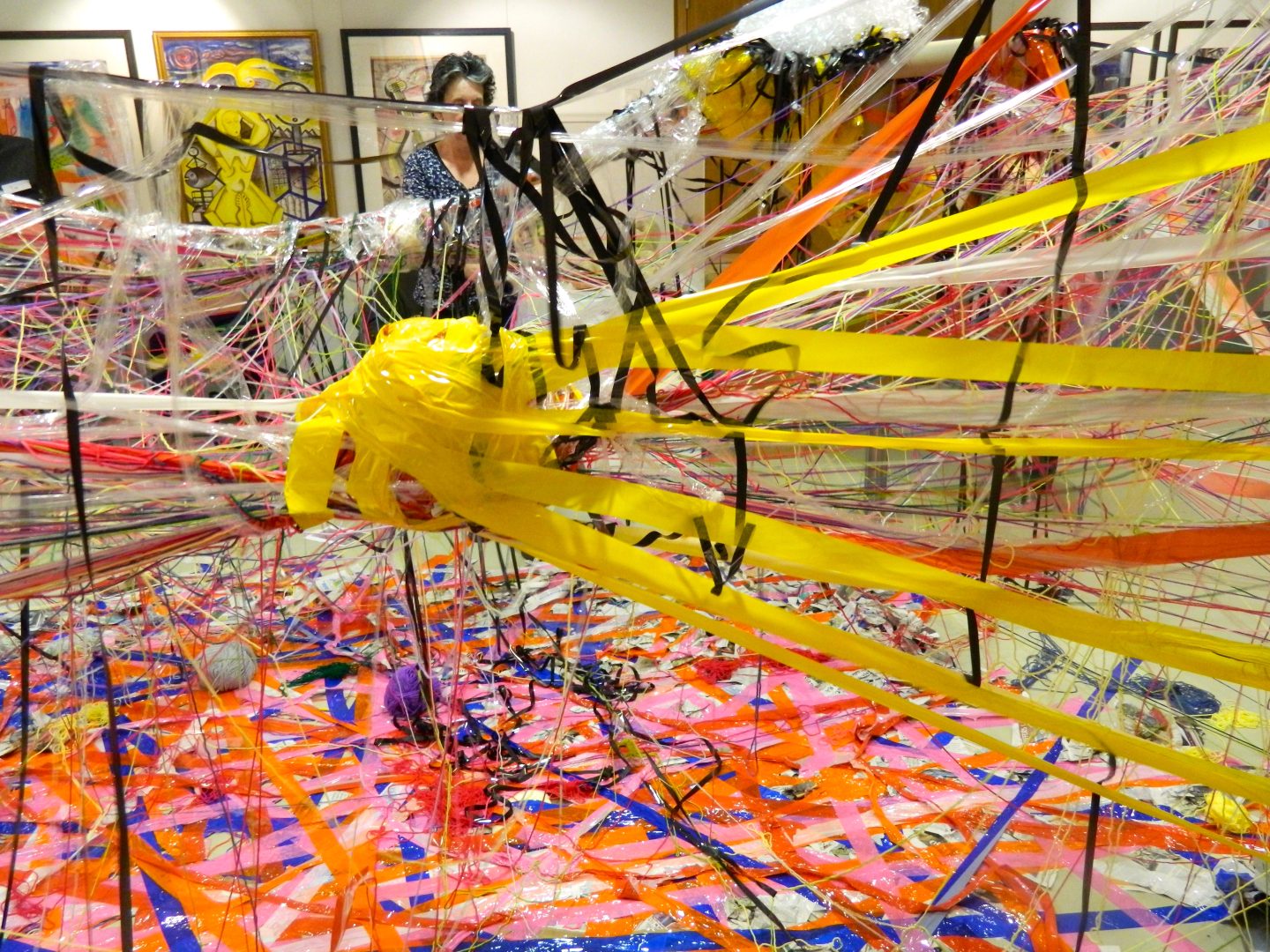 An installation artwork made up of layer of coloured tape on the floor, and tape and string binding over structures.