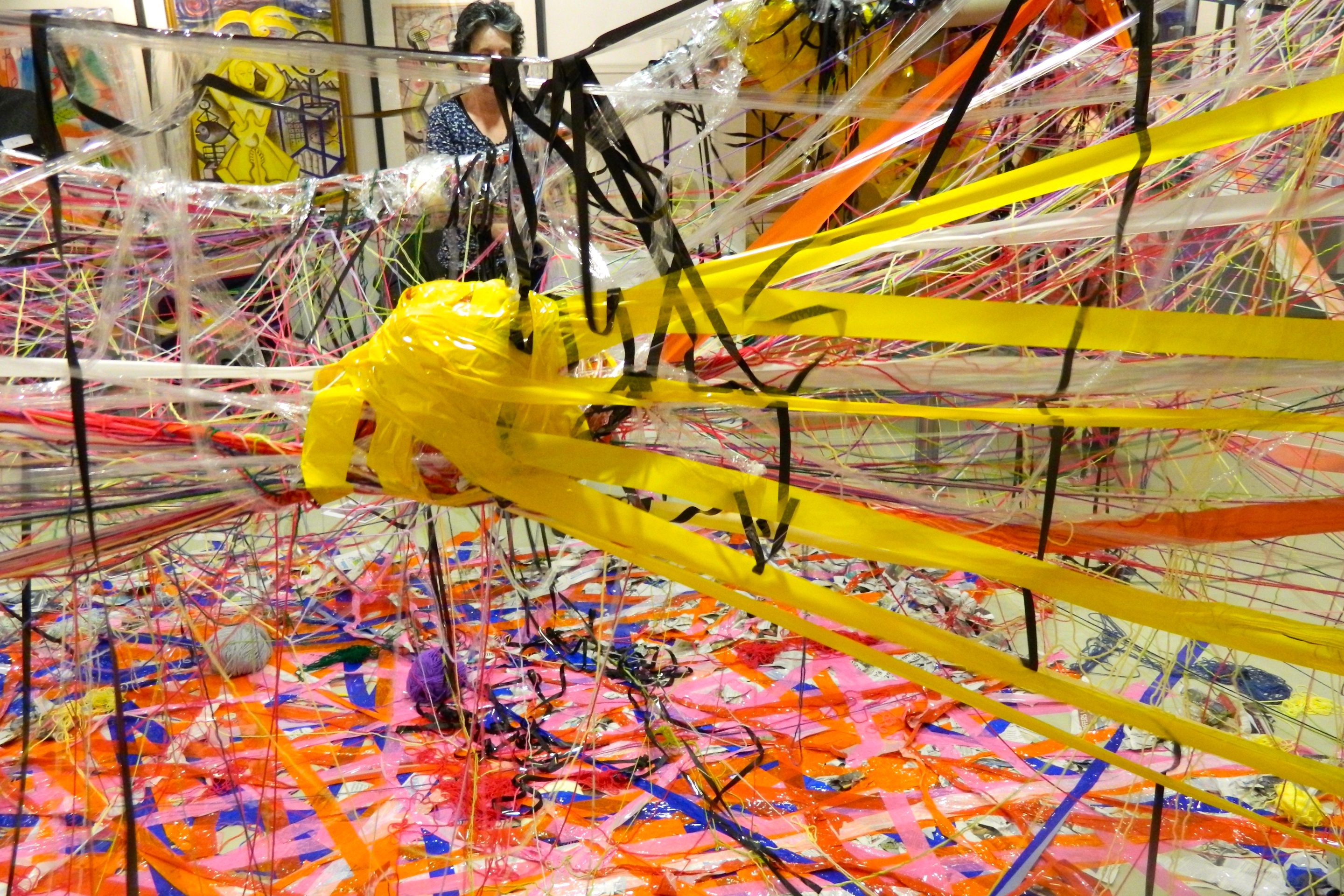 An installation artwork made up of layer of coloured tape on the floor, and tape and string binding over structures.