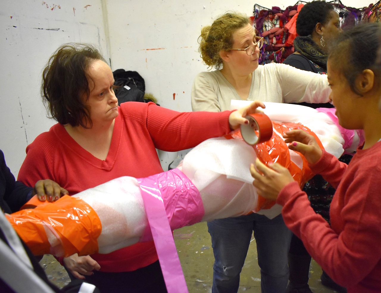 Artist Linda Bell and participants binding a foam sculpture in coloured tape during a workshop.