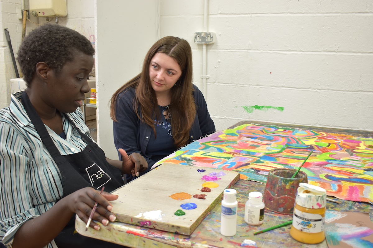 Two people sat at a table talking and looking at an artwork.
