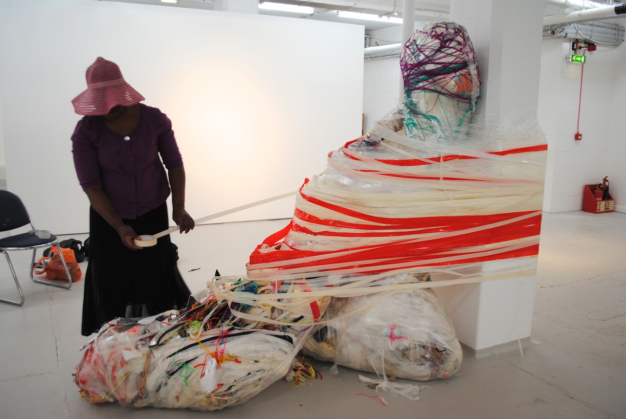 Artist Nnena Kalu binding a sculpture to a column in a gallery space.