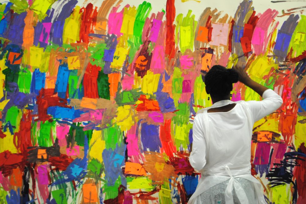 Mary Ogunleye painting a large colourful piece of different rectangular patches.