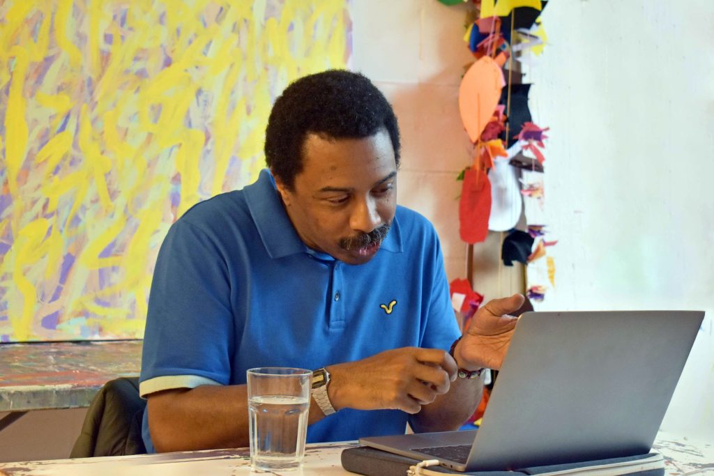 ActionSpace artist Thompson Hall sits in front of a laptop wearing a blue shirt and looking at the screen.