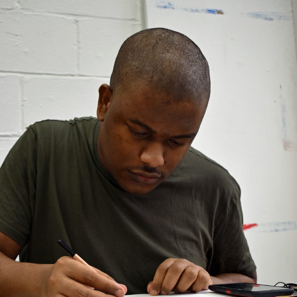 Artist Shaquille Oyeyinka drawing at a table.