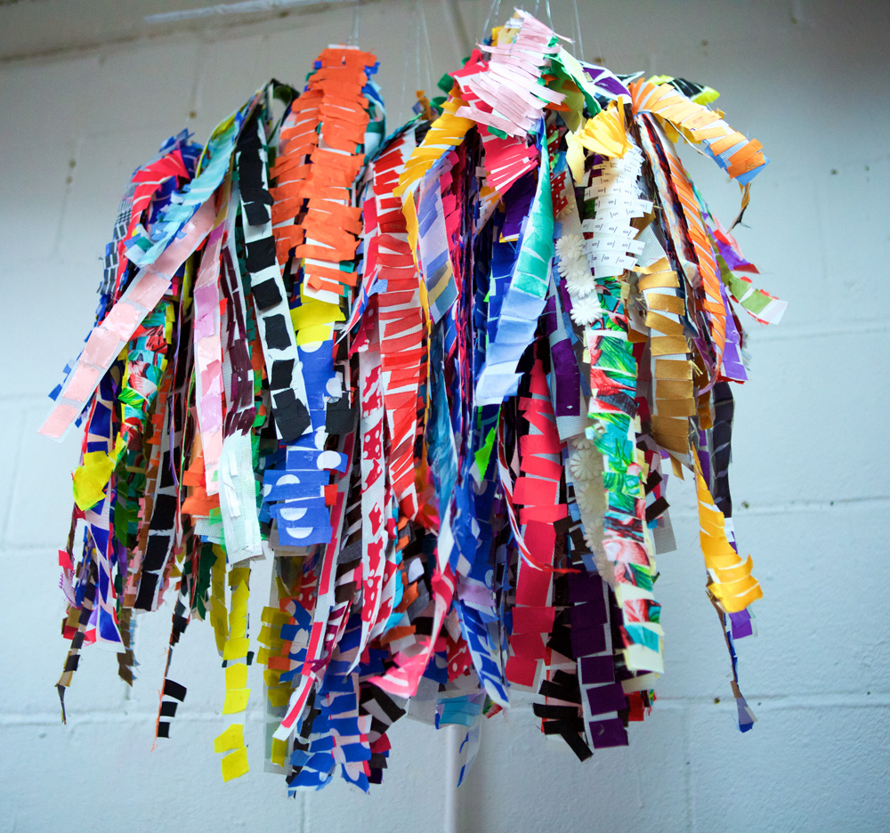 An artwork made of colourful strips of paper hangs from a ceiling.