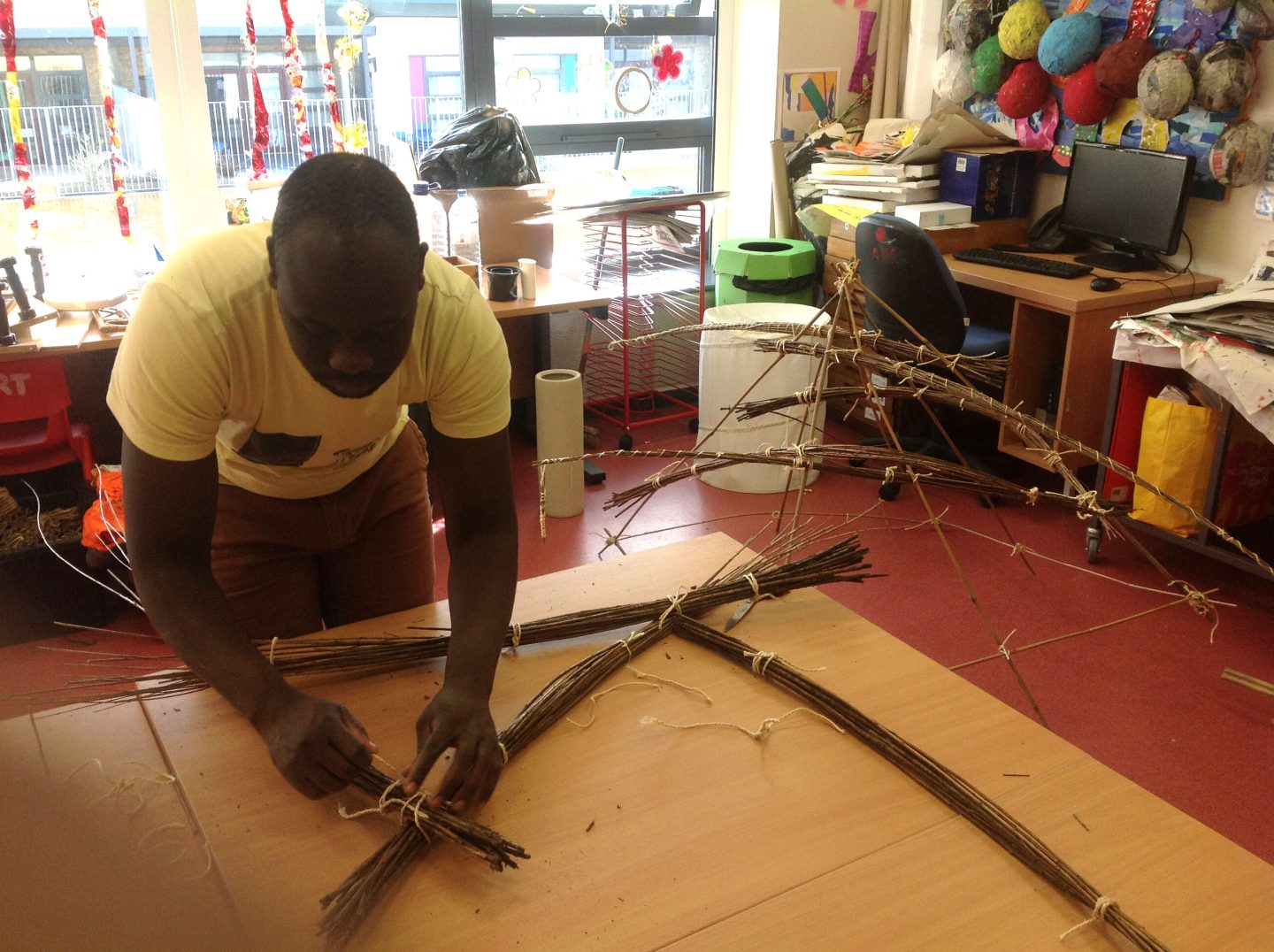 Artist Andrew Omoding tying bundles of willow sticks into a sculpture during a workshop at The Village School.